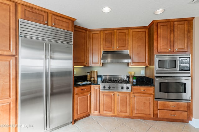 kitchen featuring built in appliances, a textured ceiling, light tile patterned floors, and dark stone counters