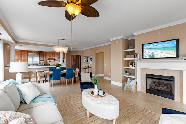 tiled living room with a tile fireplace, crown molding, ceiling fan with notable chandelier, and built in features