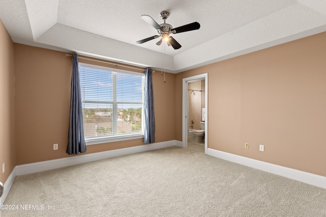 unfurnished bedroom featuring ensuite bathroom, a raised ceiling, a textured ceiling, and ceiling fan