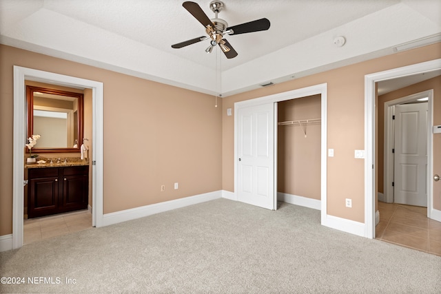 unfurnished bedroom with a closet, light carpet, ensuite bathroom, and ceiling fan