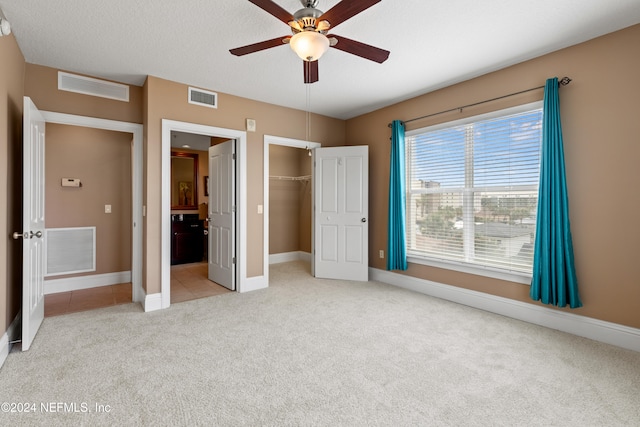 unfurnished bedroom with a spacious closet, ceiling fan, a textured ceiling, and light colored carpet