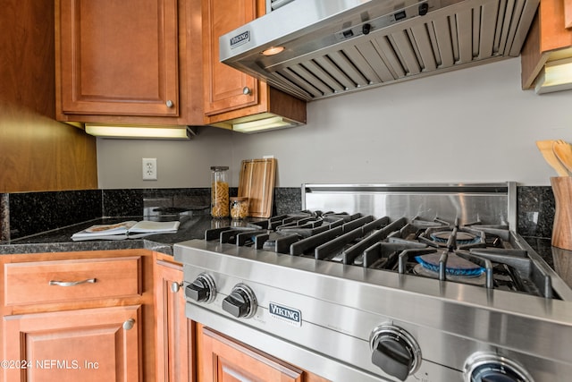 kitchen with extractor fan, dark stone counters, and stainless steel stove