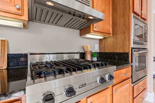 kitchen with appliances with stainless steel finishes, dark stone counters, and range hood