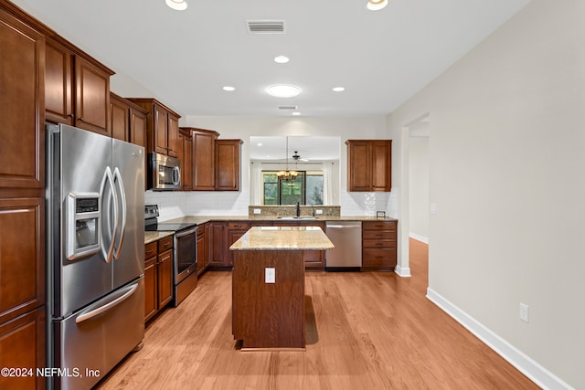 kitchen with a kitchen island, light stone countertops, light hardwood / wood-style flooring, sink, and stainless steel appliances