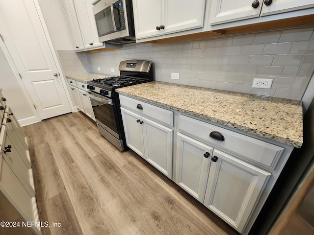 kitchen featuring tasteful backsplash, light stone counters, light hardwood / wood-style floors, white cabinets, and appliances with stainless steel finishes