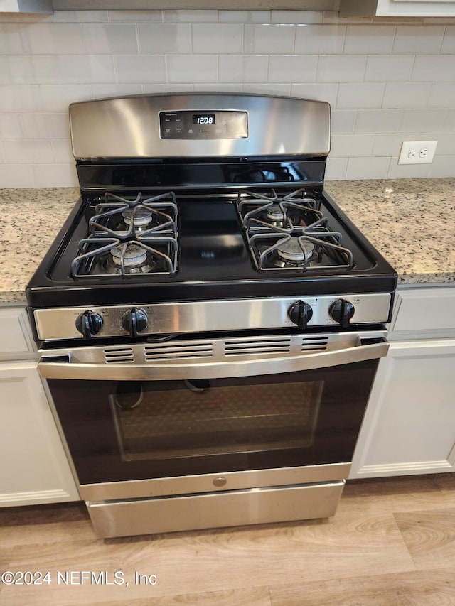 details with light stone countertops, white cabinetry, backsplash, and stainless steel range with gas stovetop