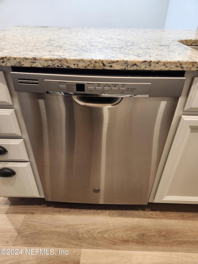 interior details with white cabinetry, stainless steel dishwasher, and light stone counters