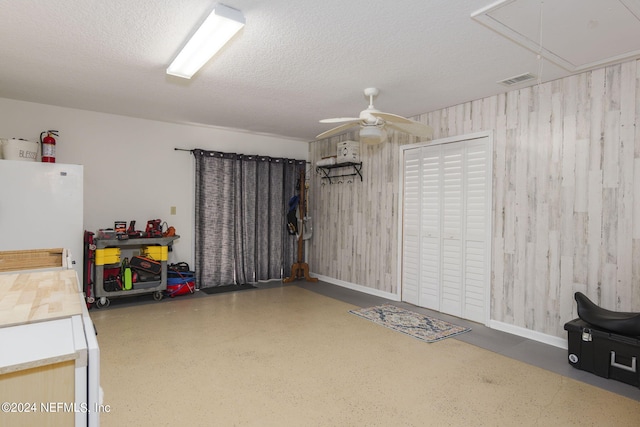 garage with white refrigerator, wood walls, and ceiling fan