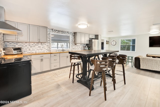 kitchen featuring stainless steel fridge, tasteful backsplash, light hardwood / wood-style floors, wall chimney exhaust hood, and wooden counters