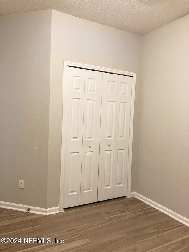 unfurnished bedroom featuring a textured ceiling, a closet, and dark hardwood / wood-style flooring