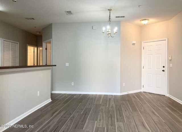 unfurnished room featuring a textured ceiling, dark hardwood / wood-style flooring, and an inviting chandelier