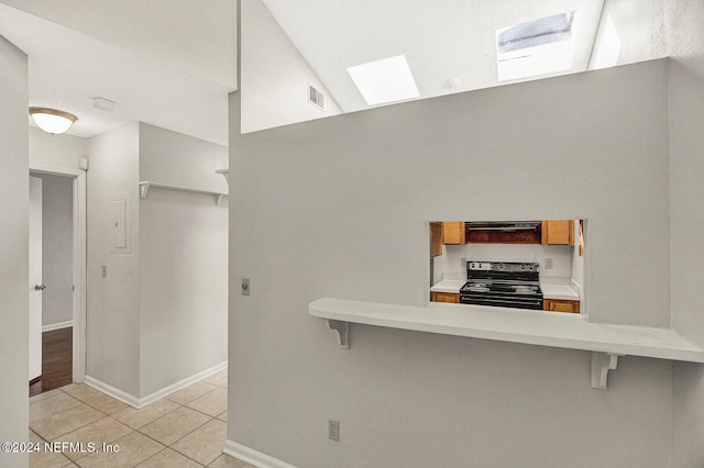 kitchen featuring extractor fan, a kitchen breakfast bar, black range with electric cooktop, light tile patterned floors, and a skylight