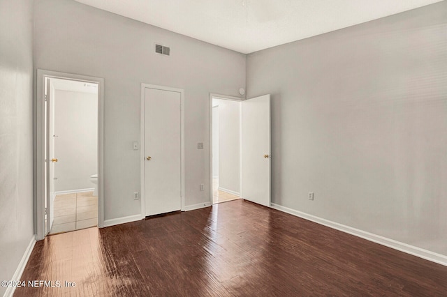 unfurnished bedroom with ensuite bathroom and dark wood-type flooring