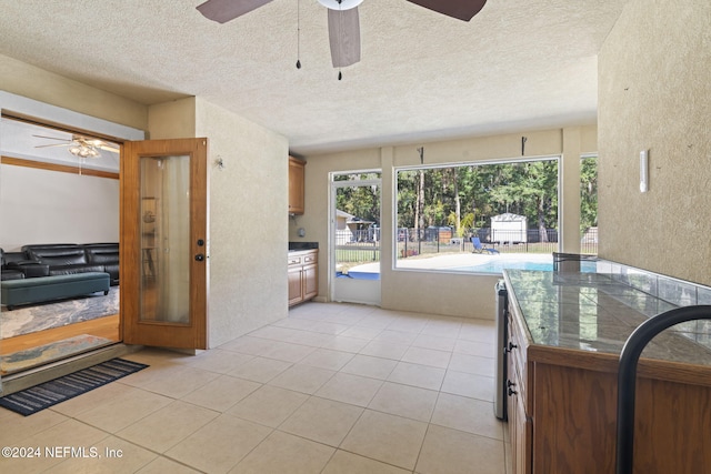 interior space featuring light tile patterned floors, ceiling fan, a textured ceiling, a textured wall, and brown cabinetry