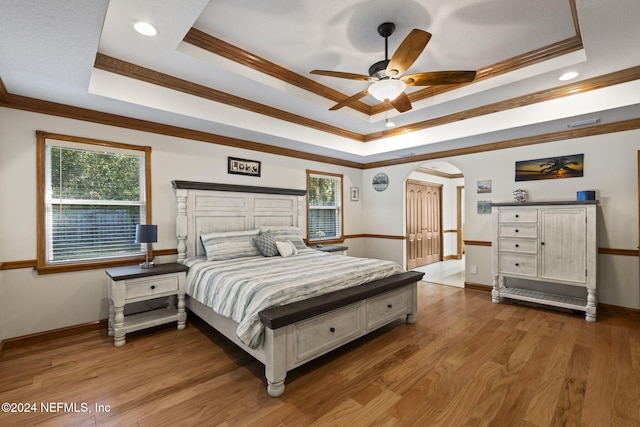 bedroom featuring arched walkways, a raised ceiling, multiple windows, and wood finished floors