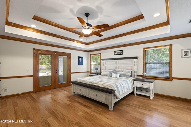 bedroom featuring access to exterior, a tray ceiling, french doors, light wood finished floors, and ornamental molding