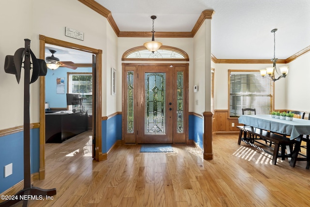 entrance foyer featuring a wainscoted wall, ornamental molding, an inviting chandelier, and light wood-style floors