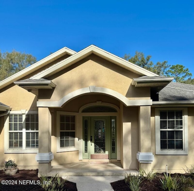 property entrance featuring a shingled roof, a porch, and stucco siding