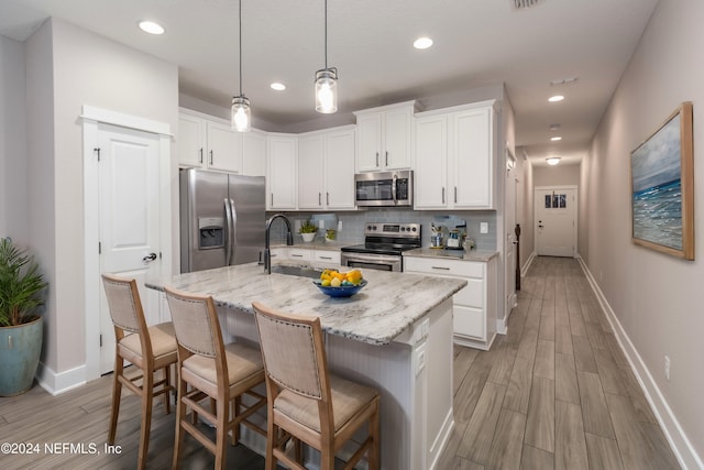 kitchen featuring appliances with stainless steel finishes, tasteful backsplash, white cabinets, a kitchen island with sink, and light stone counters