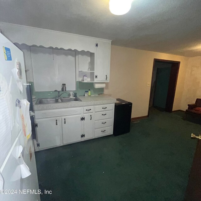 kitchen with white cabinets, a textured ceiling, dark carpet, sink, and white refrigerator