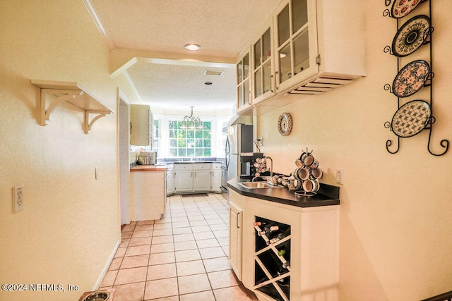 kitchen with a textured ceiling, white cabinets, light tile patterned flooring, and sink