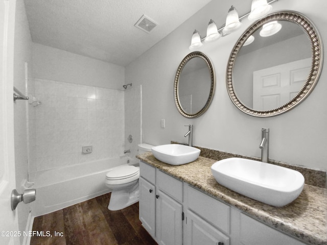 full bathroom featuring toilet, tiled shower / bath, a textured ceiling, vanity, and hardwood / wood-style floors