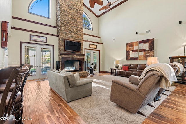 living room featuring french doors, ceiling fan, wood-type flooring, high vaulted ceiling, and a stone fireplace