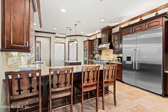 kitchen with appliances with stainless steel finishes, backsplash, light stone counters, extractor fan, and a kitchen island