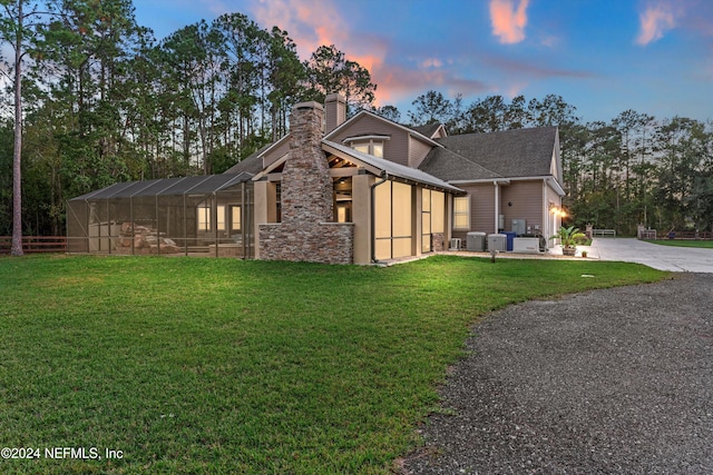 back house at dusk with a lawn and glass enclosure