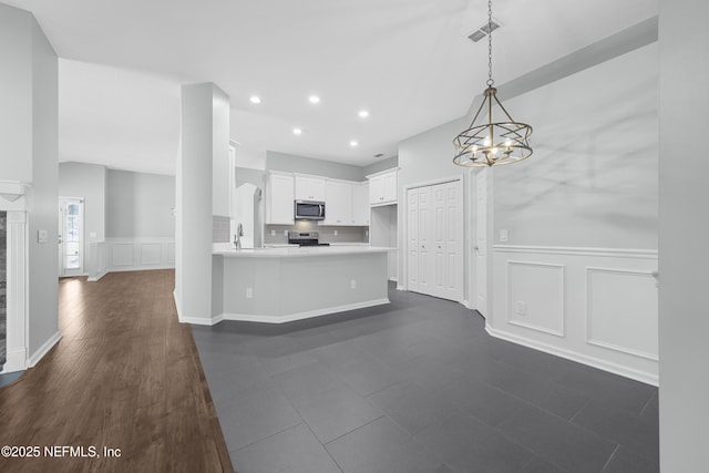 kitchen with an inviting chandelier, white cabinetry, kitchen peninsula, appliances with stainless steel finishes, and pendant lighting