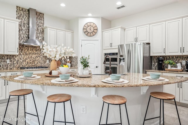 kitchen with decorative backsplash, appliances with stainless steel finishes, wall chimney range hood, white cabinets, and a center island