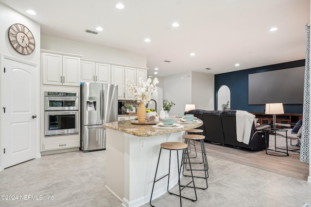 kitchen with a kitchen bar, light stone counters, stainless steel appliances, a kitchen island with sink, and white cabinetry