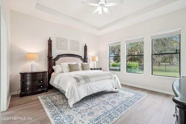 bedroom featuring a raised ceiling, multiple windows, ceiling fan, and light hardwood / wood-style floors