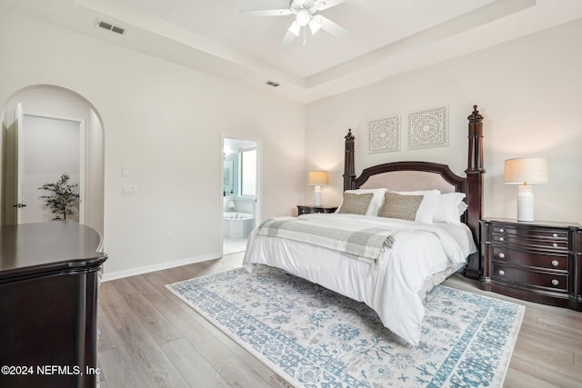 bedroom with ceiling fan, a raised ceiling, connected bathroom, and light hardwood / wood-style flooring