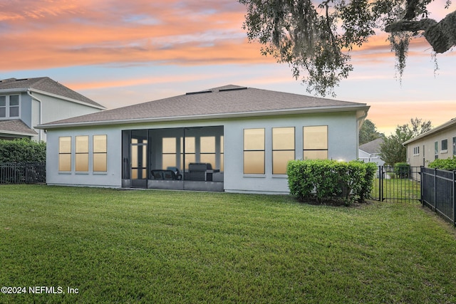 back house at dusk with a sunroom and a yard