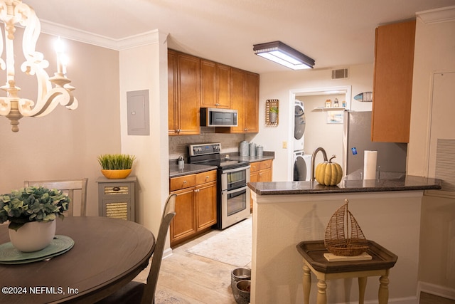 kitchen with kitchen peninsula, stacked washing maching and dryer, stainless steel appliances, and crown molding