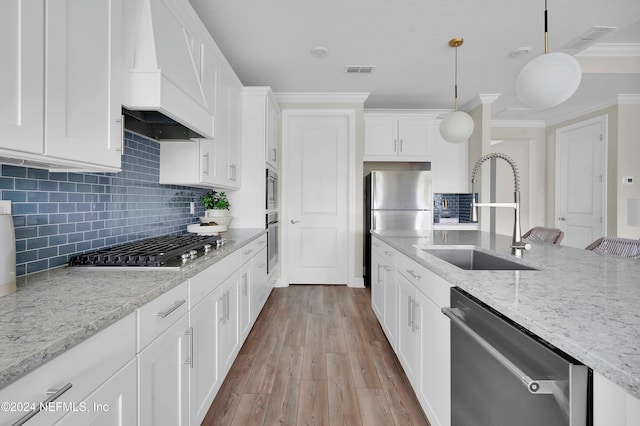 kitchen with appliances with stainless steel finishes, sink, light wood-type flooring, hanging light fixtures, and custom exhaust hood