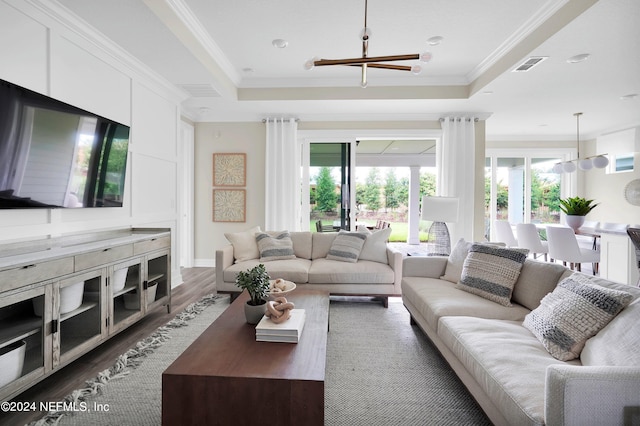 living room featuring crown molding, a raised ceiling, a notable chandelier, and dark hardwood / wood-style flooring