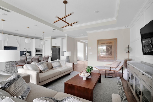 living room with a tray ceiling, ornamental molding, sink, a notable chandelier, and dark hardwood / wood-style flooring