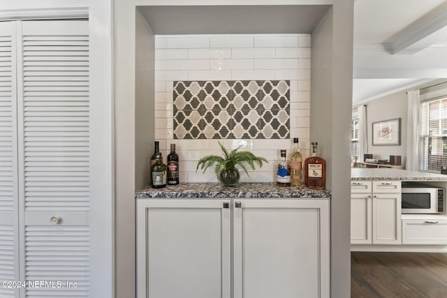 bar with crown molding, backsplash, dark hardwood / wood-style floors, white cabinets, and dark stone countertops