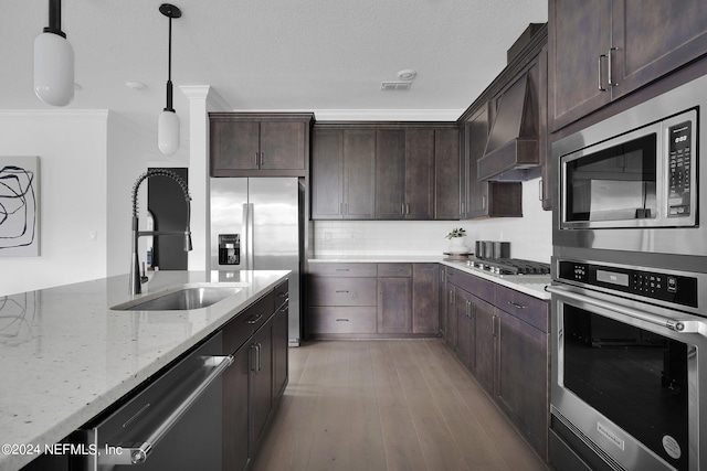 kitchen with appliances with stainless steel finishes, pendant lighting, light hardwood / wood-style floors, dark brown cabinetry, and light stone counters