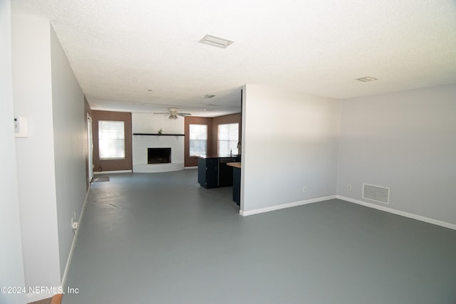 unfurnished living room featuring a textured ceiling, a brick fireplace, plenty of natural light, and ceiling fan