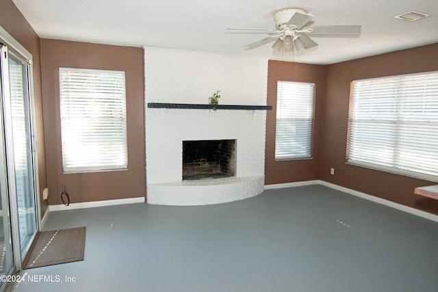 unfurnished living room with ceiling fan, a fireplace, a healthy amount of sunlight, and a textured ceiling