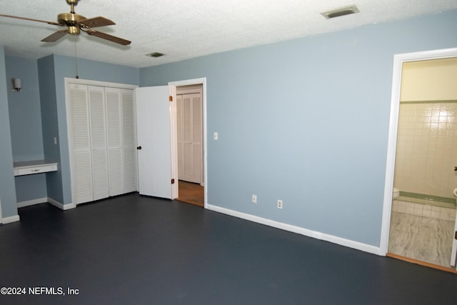 unfurnished bedroom with ceiling fan, built in desk, ensuite bathroom, and a textured ceiling