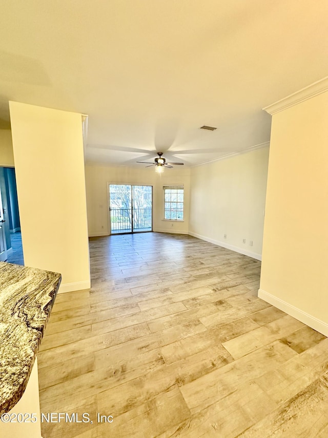 spare room with crown molding, visible vents, a ceiling fan, light wood-type flooring, and baseboards