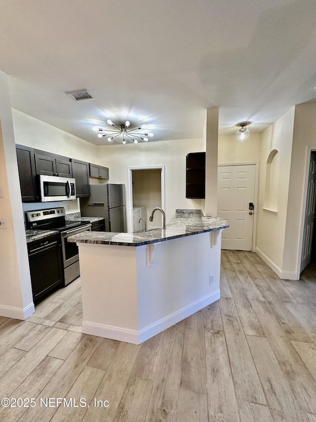 kitchen with visible vents, dark stone counters, a breakfast bar, a peninsula, and stainless steel appliances