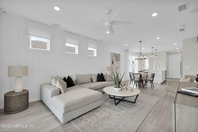 living room featuring sink, ceiling fan with notable chandelier, light hardwood / wood-style floors, and wooden walls