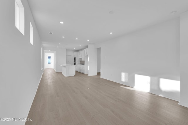 unfurnished living room with a sink, baseboards, light wood-style flooring, and recessed lighting