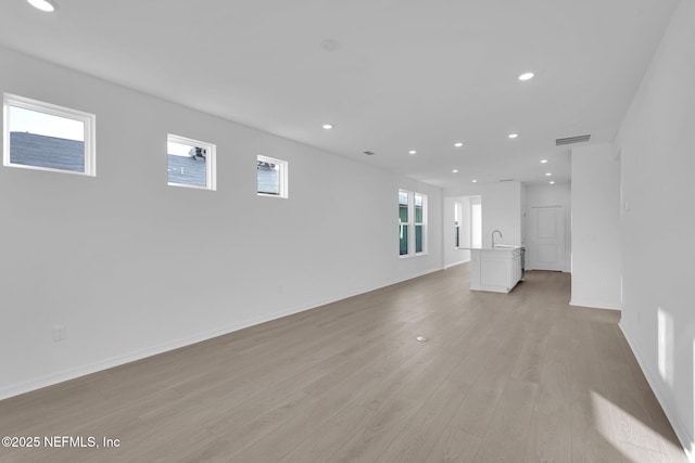 unfurnished living room with baseboards, visible vents, recessed lighting, a sink, and light wood-style floors