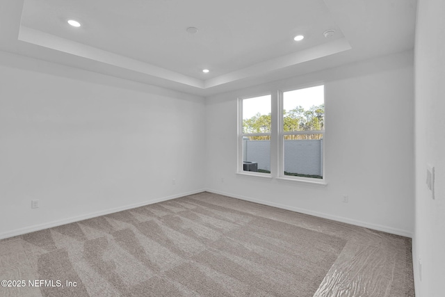 carpeted spare room featuring a raised ceiling and baseboards